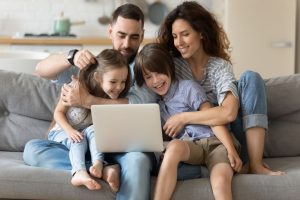 a family picture of 4 in a living room looking at a laptop screen.