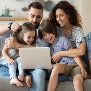 a family picture of 4 in a living room looking at a laptop screen.